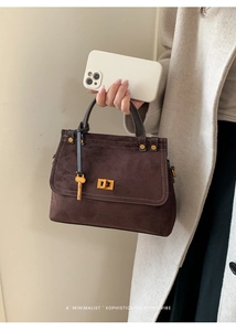 Detail of retro dark brown suede handbag featuring gold twist lock and key charm detail