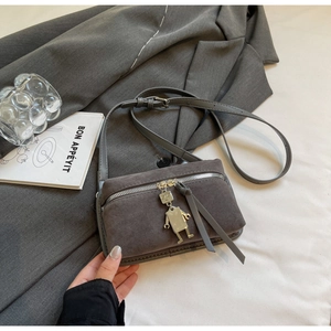 Close-up of gray suede crossbody bag with robot pendant and silver zipper detail