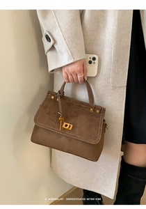 Detail of retro brown suede handbag featuring golden twist lock and contrast stitching