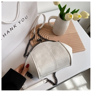 Detail of white quilted leather shell bag with metal clasp on a wooden tray