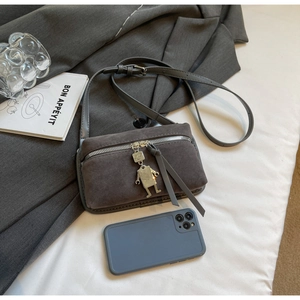 Detail of grey faux suede crossbody bag featuring silver hardware and a robot charm