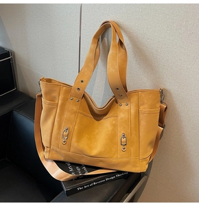Detail view of the mustard yellow tote bag with metallic buckles on a black leather seat