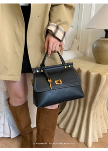 Detail of black suede-like small square bag with white contrast stitching and gold clasp