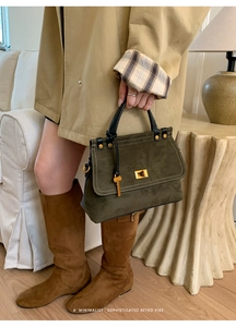 Olive green suede handbag with golden buckle shown held by a model in a trench coat
