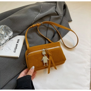 Detail of yellow suede crossbody bag with silver robot charm and metal zipper accent