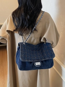 Quilted dark blue denim shoulder bag with silver chain strap shown on a khaki trench coat