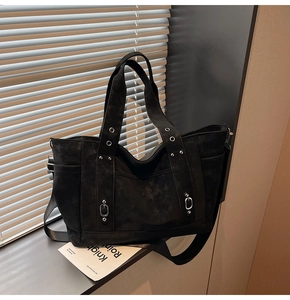 Close-up of black suede tote bag featuring silver studs and industrial metal eyelets