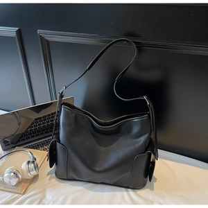 Detail of large black PU leather tote bag with side flap pockets and wide shoulder strap