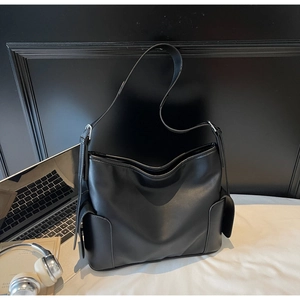 Detail of black PU leather tote bag with side pockets and wide strap in office setting