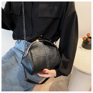 Detailed close-up of retro black shell bag with white cross-stitching and chain strap
