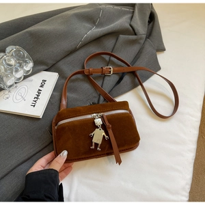Close-up of brown suede crossbody bag with metal zipper and robot-shaped pendant charm