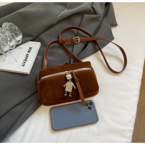 Close-up of brown suede crossbody bag featuring silver zipper and robot metal charm