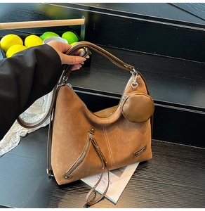 Detail of a brown matte hobo bag featuring decorative zippers and a round coin purse charm