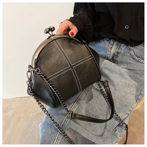 Detail of black retro shell bag showing white cross stitching and metal kiss-lock closure