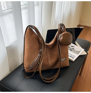 Detail of brown suede tote bag with zipper and round coin purse on a soft bench