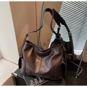 Detail of dark brown faux leather tote bag with wide strap on black wooden surface