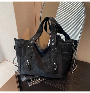 Close-up of black suede tote bag with silver metal eyelets and decorative buckles