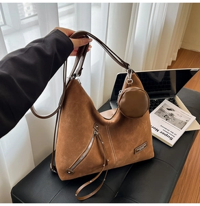 Detail of a brown suede hobo bag with tassel zippers and a mini round coin purse charm