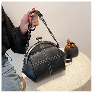 Detail view of the black shell bag featuring white cross stitching and metal kiss-lock closure
