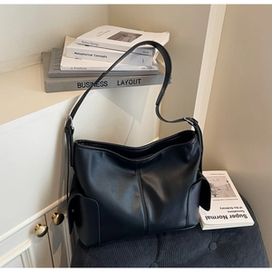 Detailed close-up of a black PU leather tote bag with large side flap pockets on books