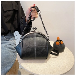 Detail of black shell crossbody bag featuring white cross-stitching and metal clasp closure