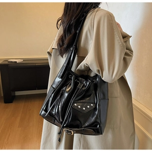 Detail view of black glossy leather bucket bag with metal rivets and drawstrings