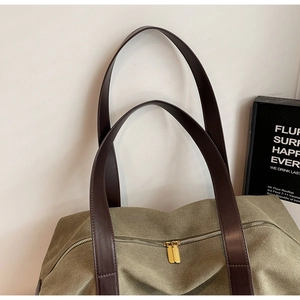 Detail of the dual golden metal zippers and brown leather handles on the olive canvas tote
