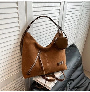 Close-up of caramel brown suede tote bag with decorative zipper and leather logo patch