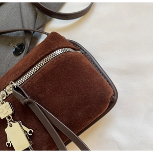 Detail of brown suede crossbody bag with silver zipper and robot metal pendant charm