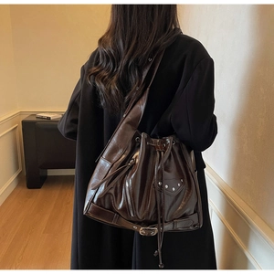 Close-up of deep brown glossy leather bucket bag with silver rivets and zippers