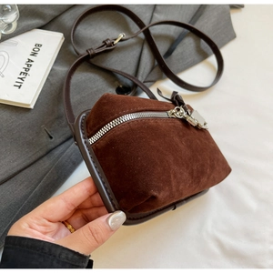 Détail d'un sac bandoulière en daim marron foncé avec fermeture éclair argentée courbe