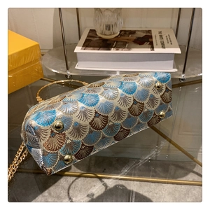 Detailed bottom view of an embroidered shell bag with gold protective studs and metal chain