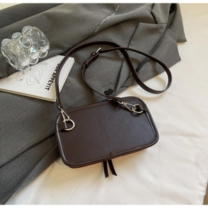 Détail du sac bandoulière en daim café avec anneau métallique et pompon sur veste