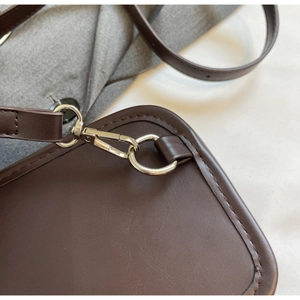Detail of dark brown faux suede bag with silver metal hook and refined stitching texture