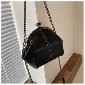 Detailed view of the black shell bag showing white cross-stitching and metal clasp closure