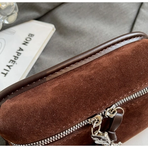 Macro shot of dark brown suede bag with silver smiley face zippers and leather piping