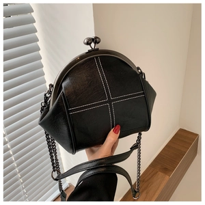 Close-up of vintage black leather shell bag with white cross stitching and metal chain