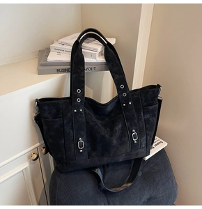 Detail of black suede tote bag with silver metal eyelets and adjustable strap