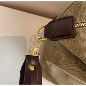Detail of military green canvas bag featuring brown leather accents and gold hardware