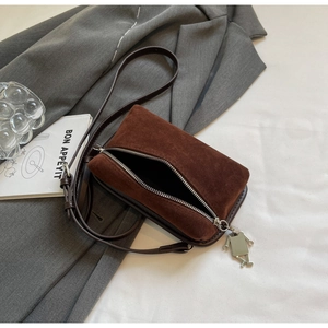 Detail of coffee brown suede crossbody bag with silver robot charm and zipper closure