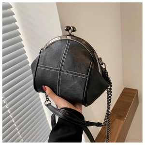 Close-up of black shell bag with white contrast stitching and metallic chain strap