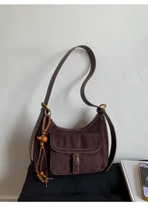 Close-up of brown suede shoulder bag with white stitching and wood bead tassel charm