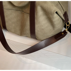 Detail view of army green canvas tote with brown leather handles and gold metal hardware