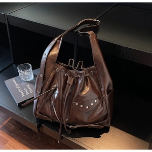 Detail view of large dark brown bucket bag with decorative metal rivets and drawstring