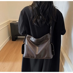 Detail of dark brown leather tote bag with side pockets worn over a black wool coat