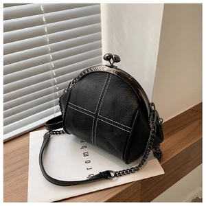 Detail of black shell crossbody bag with white cross stitching and metal chain strap
