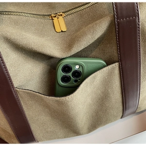 Detail of olive canvas tote bag with brown leather handles and a smartphone in the outer pocket