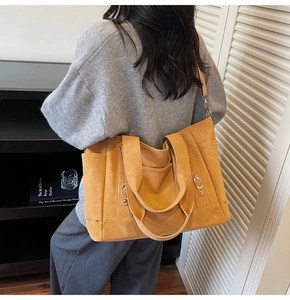 Detail of a large mustard tote bag with dual handles and side pocket for daily commute