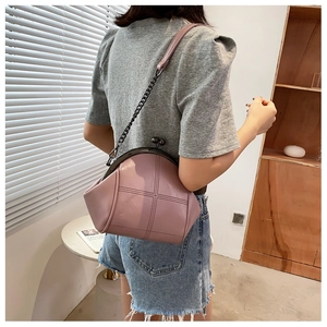 Detail of mauve PU leather shell bag with metal clasp and chain strap on a model