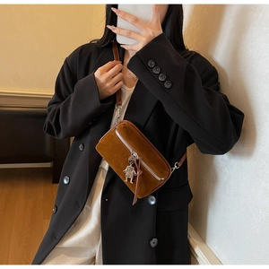 Detail view of brown suede crossbody bag with a robot pendant and slim shoulder strap